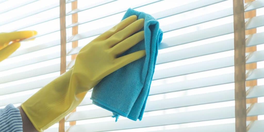 Closed white aluminum blinds on a window ledge with three small decorative vases in blue, teal, and white